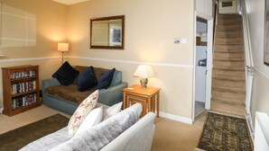 A living room with a sofa, a coffee table, a bookshelf, and a staircase leading to an upper floor. - Amelie Cottage (Beaumaris)