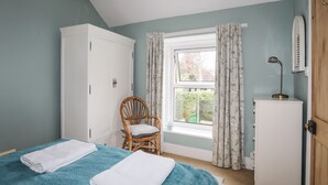 A bedroom with two beds, a wardrobe, a chair, a window with curtains, and a desk with a lamp. - Amelie Cottage (Beaumaris)