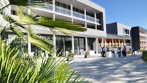 Un edificio moderno con un amplio espacio exterior, ventanas grandes y un grupo de personas reunidas cerca de la entrada.