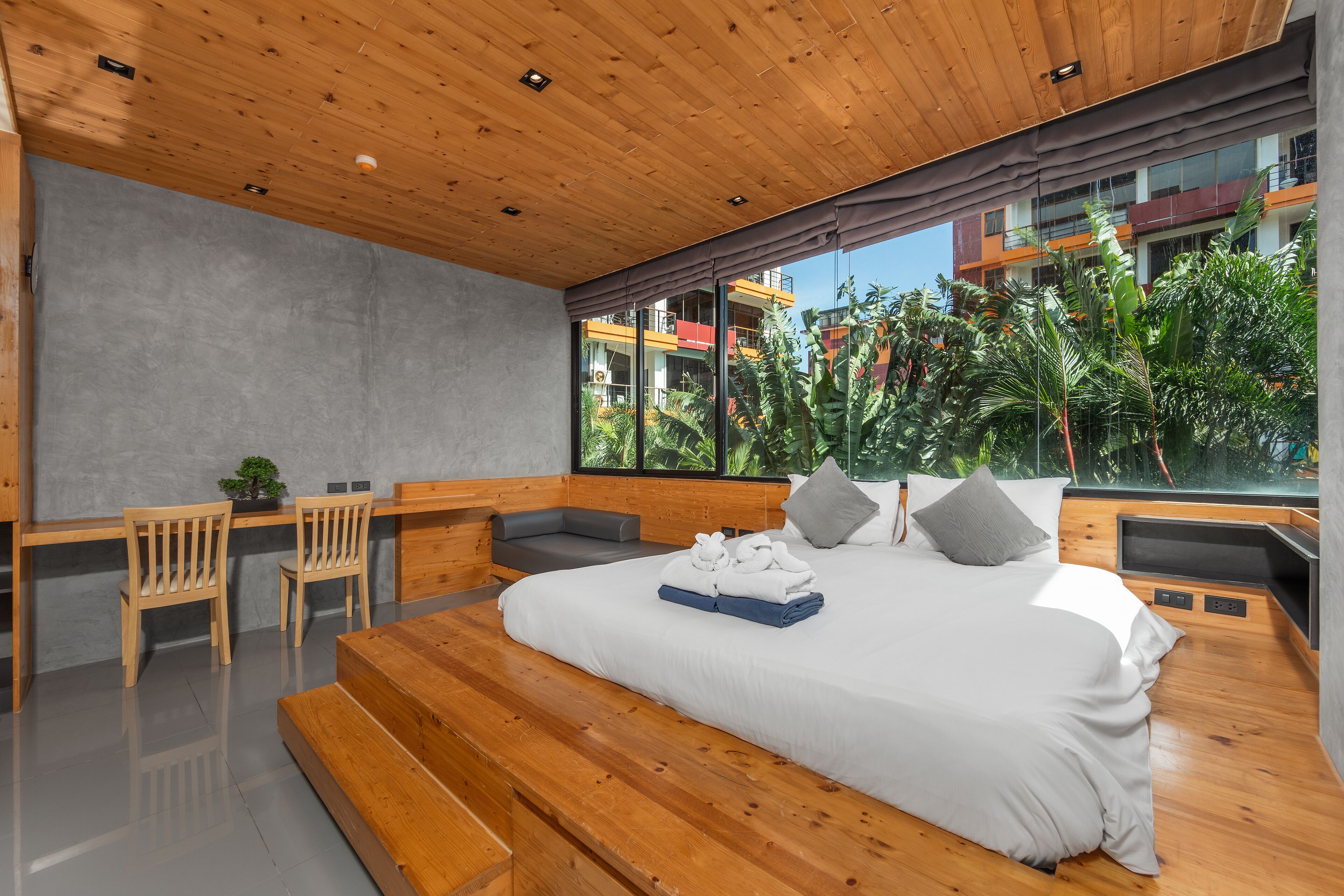 A modern bedroom with a wooden ceiling, large windows, a bed, a desk, and a seating area.