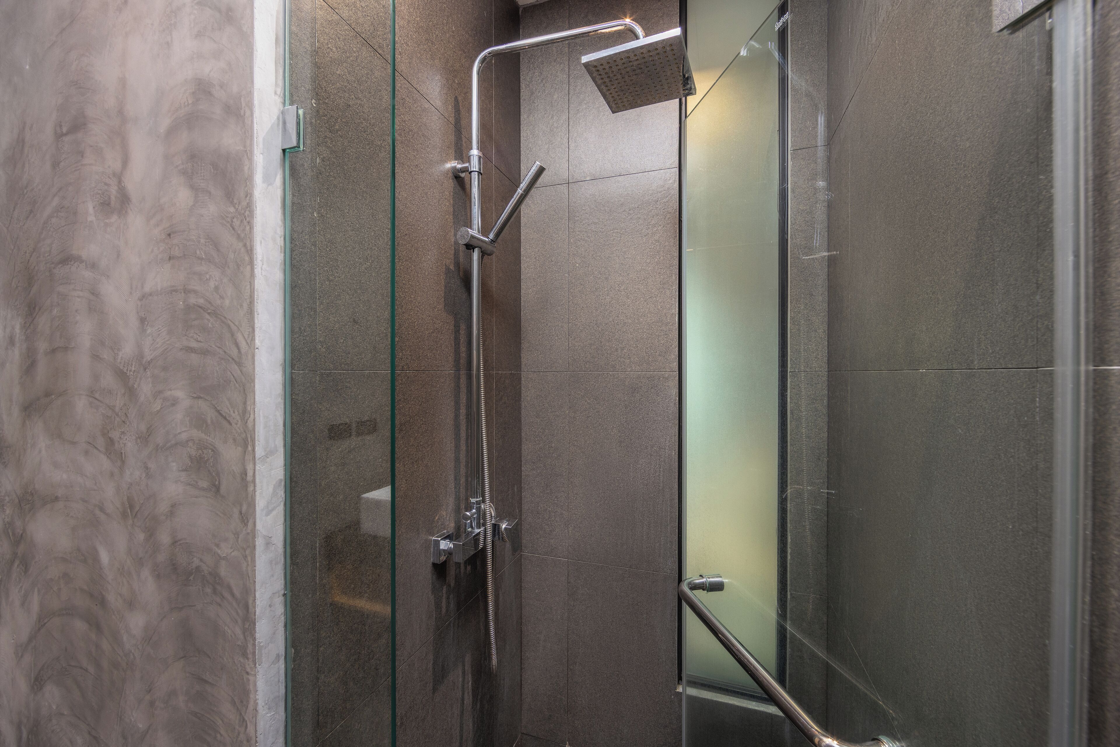 Une douche fermée par des parois en verre, dotée d’un pommeau de douche à main et d’un robinet mural.