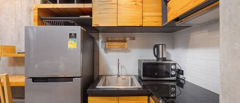 Una cocina compacta con armarios de madera, un refrigerador de acero inoxidable, un microondas y un lavamanos.