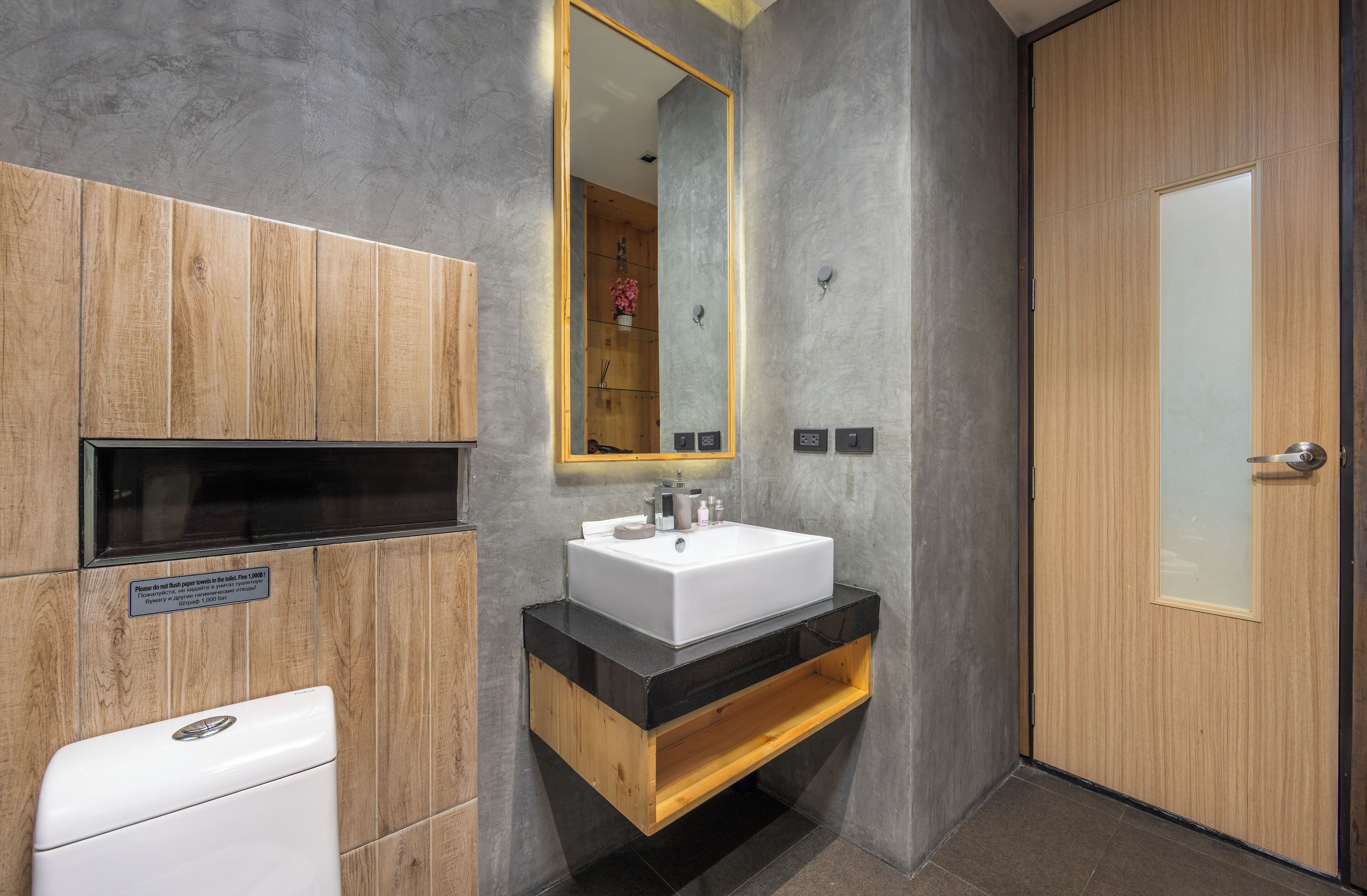 A modern bathroom with a wooden vanity, a white sink, and a large mirror.