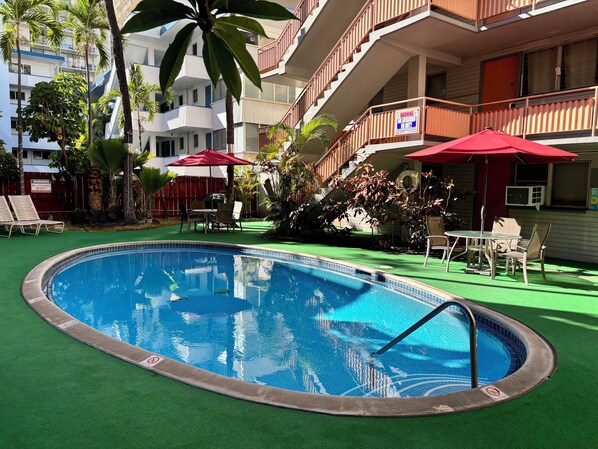 A swimming pool with a green deck, surrounded by lounge chairs and umbrellas.
