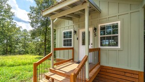 A wooden porch with a railing, a door, and two windows.