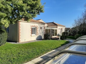 Une maison à deux étages, avec un toit en tuiles, un petit porche à l’avant et une pelouse bien entretenue.