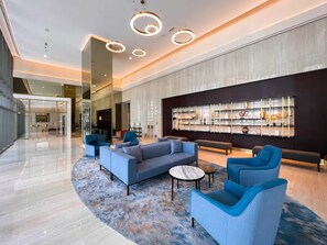 A spacious lobby with a modern blue sofa set, a marble floor, and a large wall with a decorative shelf.