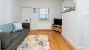 Ein Wohnzimmer mit grauem Sofa, Fernseher und Heizkörper.