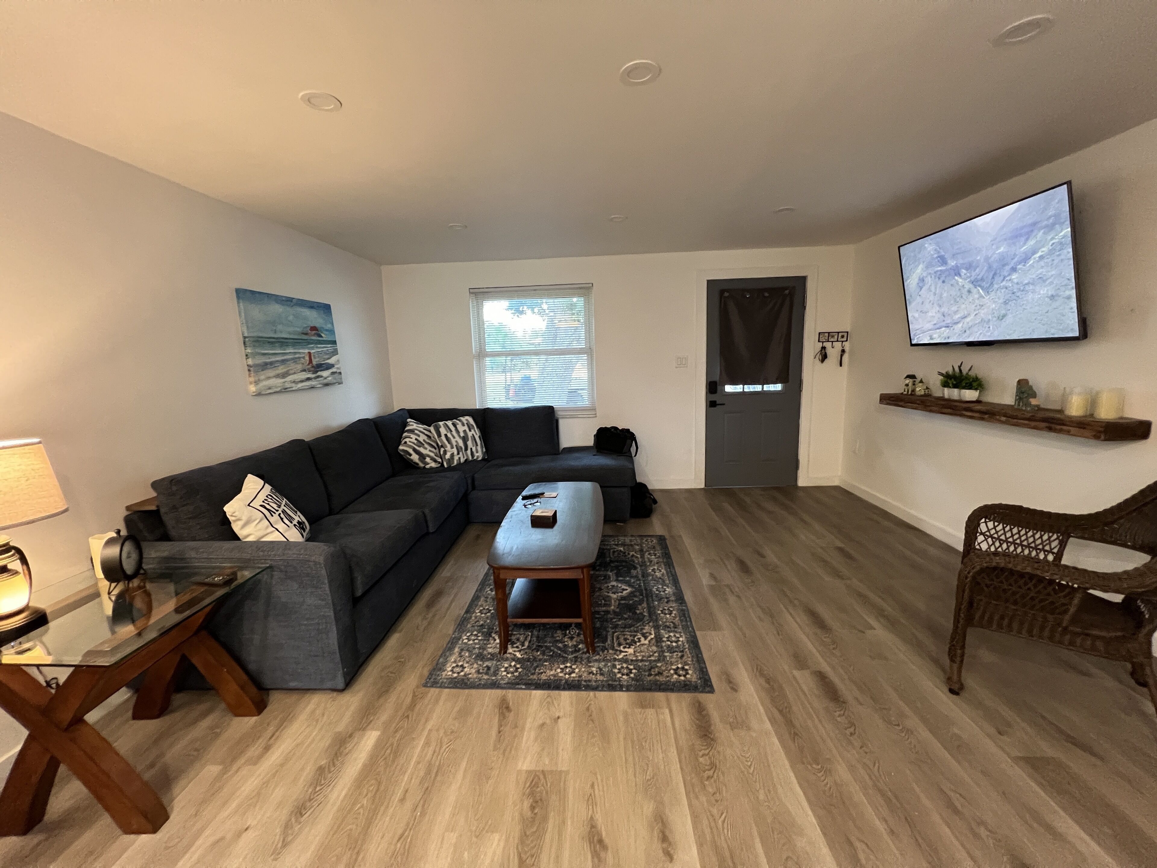 A living room with a sectional sofa, a coffee table, a TV mounted on the wall, and a wooden floor.