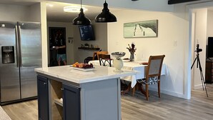 A modern kitchen with a central island, stainless steel appliances, pendant lighting, and a dining area with a table and chairs.