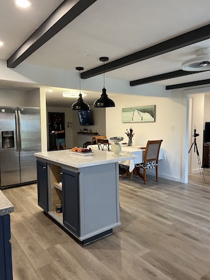 A modern kitchen with a central island, stainless steel appliances, pendant lighting, and a dining area with a table and chairs. - Our Florida Dream Awaits: Sun-kissed Retreat, Family-Friendly Oasis (Port Charlotte)