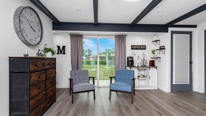 A modern living room with a large clock, two armchairs, a wooden cabinet, and a coffee station.