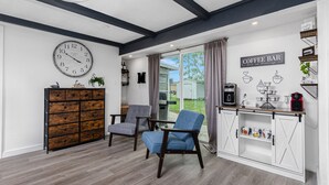 A room with a wooden cabinet, two chairs, a coffee bar with mugs, and a clock on the wall.