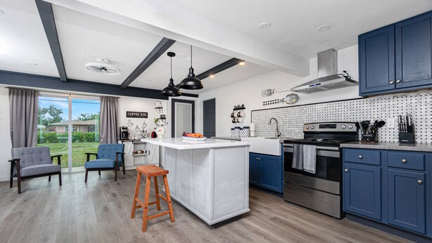 A modern kitchen with blue cabinets, a central island, and a dining area with two chairs.