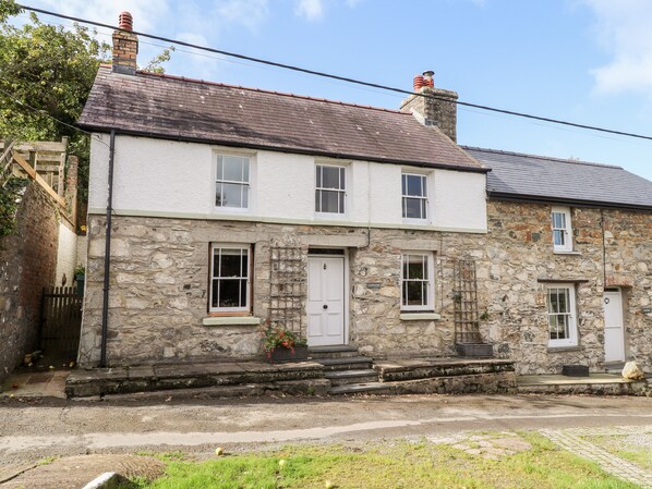 A stone house with a white door, multiple windows, and a small porch area.