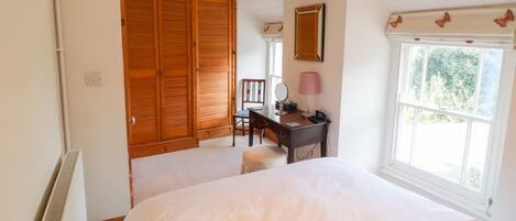Un dormitorio con una cama grande, armario de madera, escritorio con lámpara y ventana con vistas a zonas verdes.