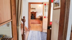 A hallway leading to a room with a wooden staircase, a rug, and a door with a picture.
