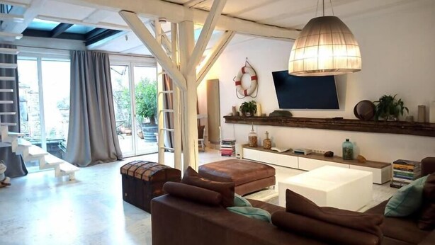 A spacious living room with a large sofa, a coffee table, and a TV mounted on a wooden shelf. There is a staircase leading to an outdoor area with a view of greenery. - SEVORAGE (Walzbachtal)