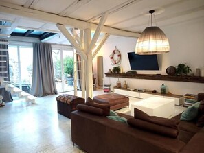 A spacious living room with a large sofa, a coffee table, and a TV mounted on a wooden shelf. There is a staircase leading to an outdoor area with a view of greenery. - SEVORAGE (Walzbachtal)