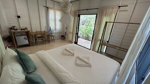 Une chambre d’hôtel avec un grand lit, un bureau et une chaise. La fenêtre offre une vue sur la verdure.