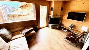 Een gezellig houten blokhutinterieur met een stenen openhaard, een bank, een leren fauteuil en een aan de muur bevestigde televisie.