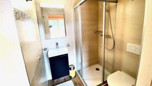 Een kleine badkamer met een douchecabine van glas, een wastafel met spiegel en een toilet.