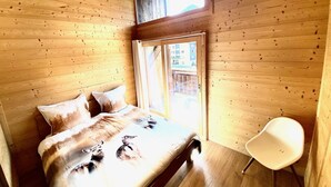 Een houten kamer met een bed, een raam en een stoel.