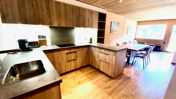 Een moderne keuken met houten kastjes, een roestvrijstalen spoelbak en een eethoek met een tafel en stoelen.