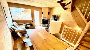 Een houten interieur met een lange eettafel, stoelen, een bank en een trap.