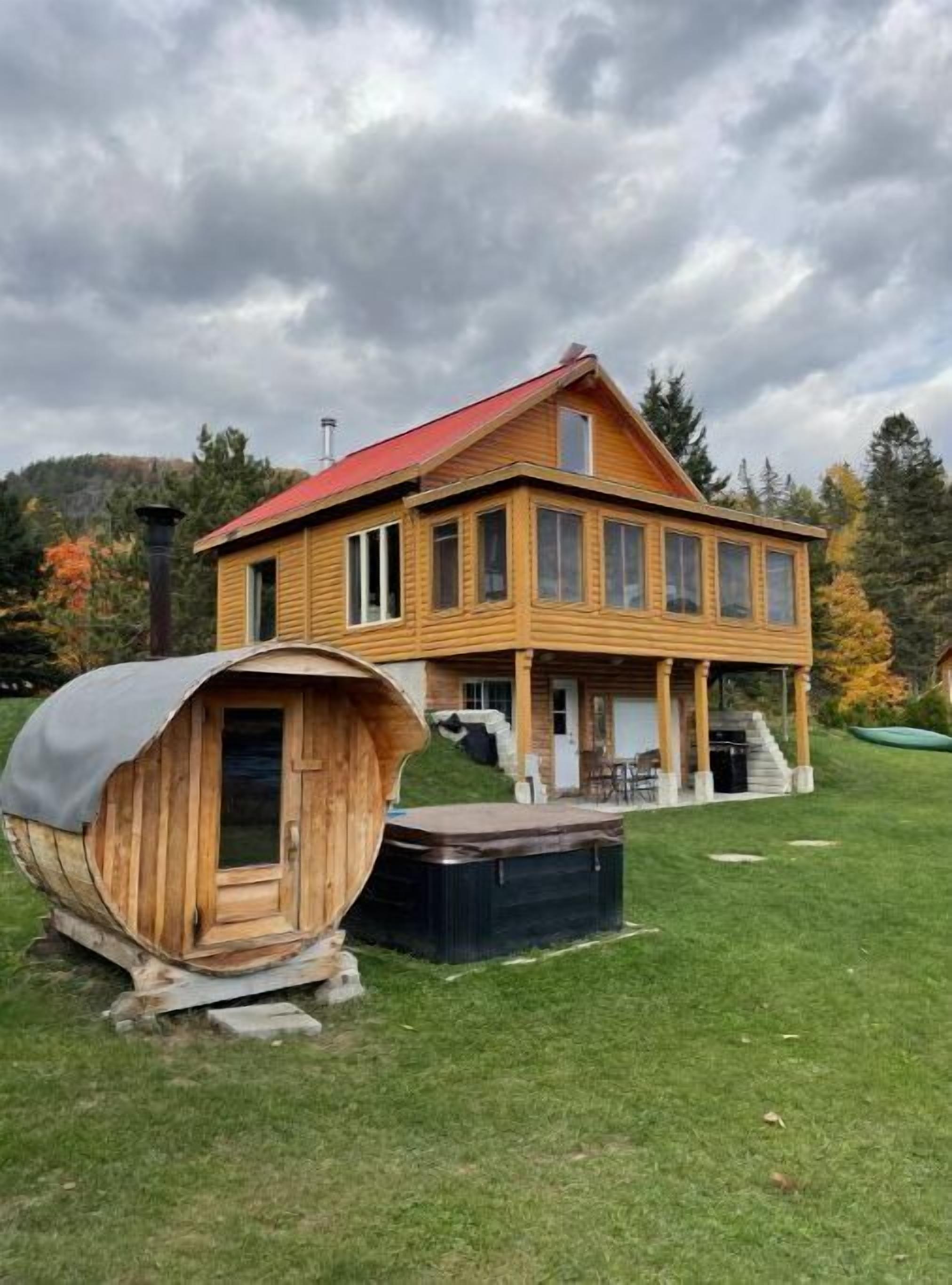 Una cabaña de madera con techo rojo, un porche cubierto y un jacuzzi al frente.