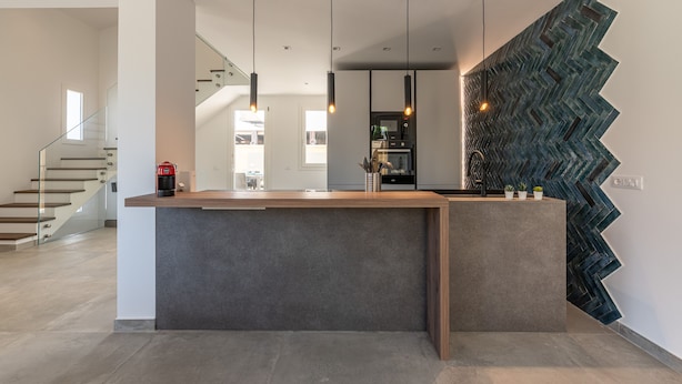 A modern kitchen with a central island, pendant lighting, and a unique zigzag wall design.