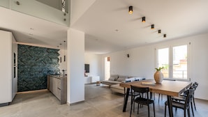 A modern kitchen with a herringbone backsplash, a dining area with a wooden table and chairs, and a living space with a sofa and a large window.