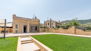 A courtyard with a stone staircase leading to a building entrance, surrounded by a well-maintained lawn and a stone wall.