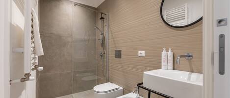 Une salle de bain moderne avec une douche à parois de verre, des toilettes blanches, un bidet et un lavabo équipé de produits de toilette.