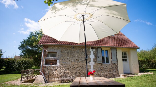 Ein Steinhaus mit rotem Ziegeldach, einer Bank und einem Picknicktisch unter einem großen Sonnenschirm.