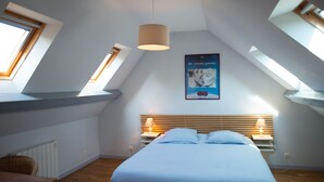 Ein Schlafzimmer mit geneigter Decke, Dachfenstern, einem Bett mit Holz-Kopfteil und einem Poster an der Wand.
