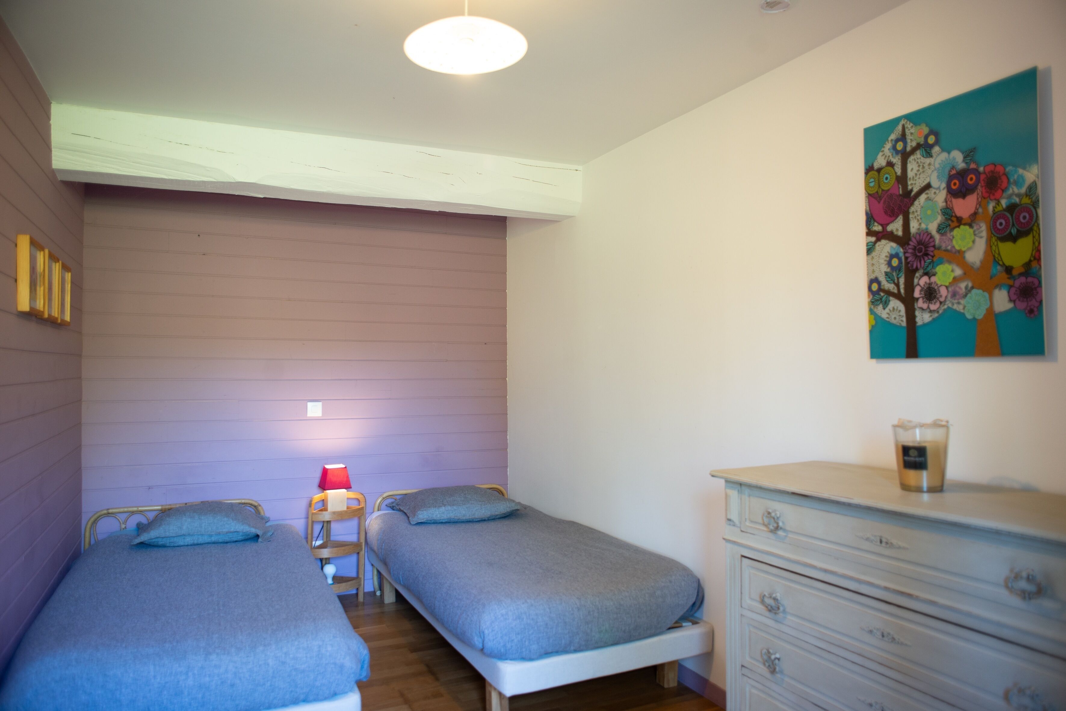 A bedroom with two single beds, a dresser, a painting, and a lamp.