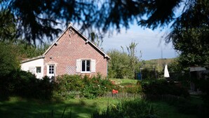 Ein Ziegelhaus mit geneigtem Dach, umgeben von einem Holzzaun und üppiger Bepflanzung.