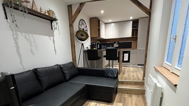 A modern living room with a sectional sofa, wooden flooring, and a kitchen in the background.