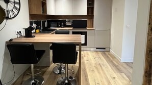 A modern kitchen with a wooden countertop, two black bar stools, a black microwave, and white cabinets.