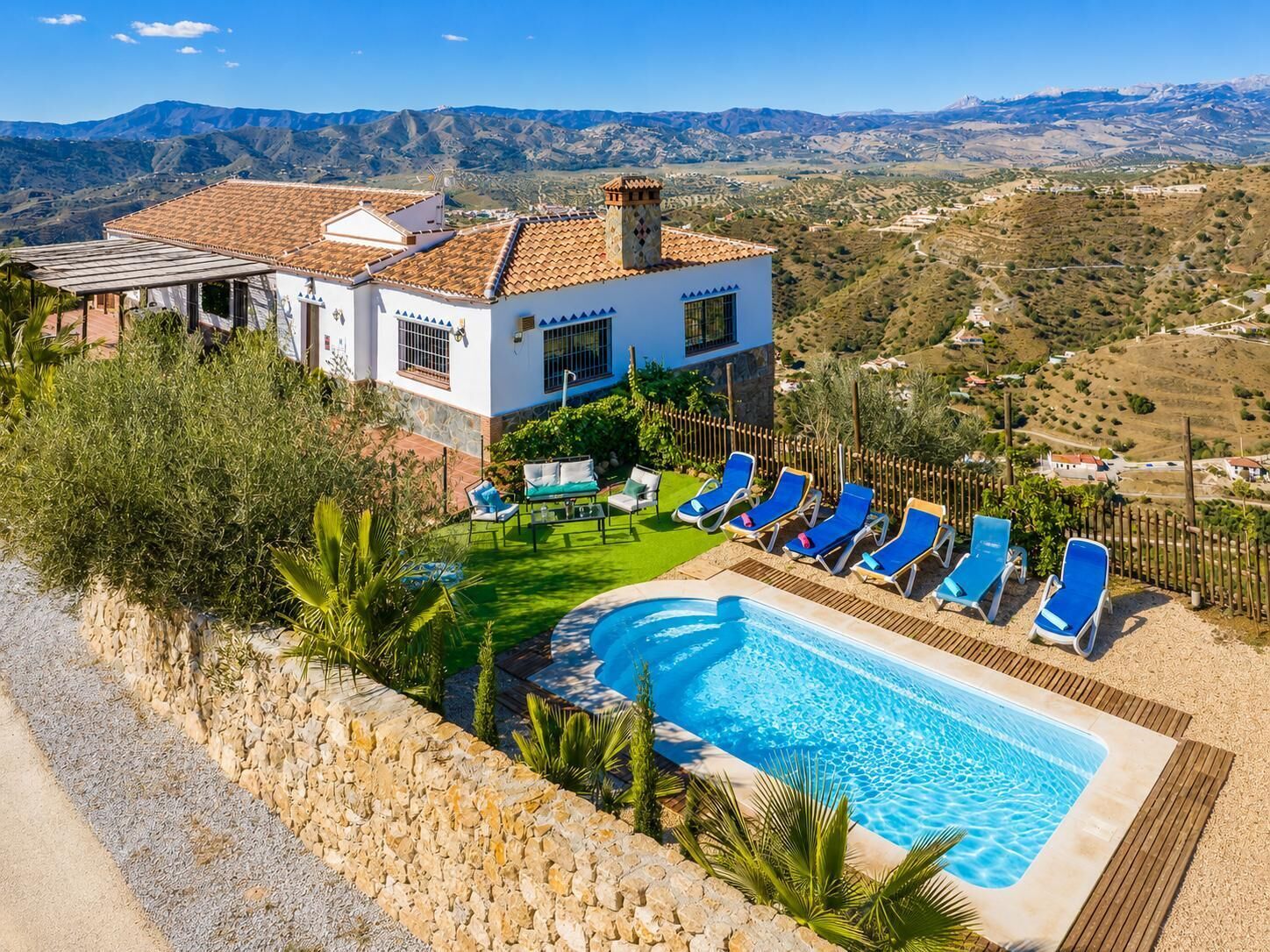 A poolside area with lounge chairs and a swimming pool, surrounded by a stone wall and greenery.