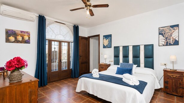 A hotel room with a bed, a wooden dresser, a ceiling fan, and a window with curtains.