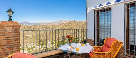 Un balcon agrémenté de meubles en osier, une table préparée pour le petit-déjeuner et une vue sur un paysage montagneux.
