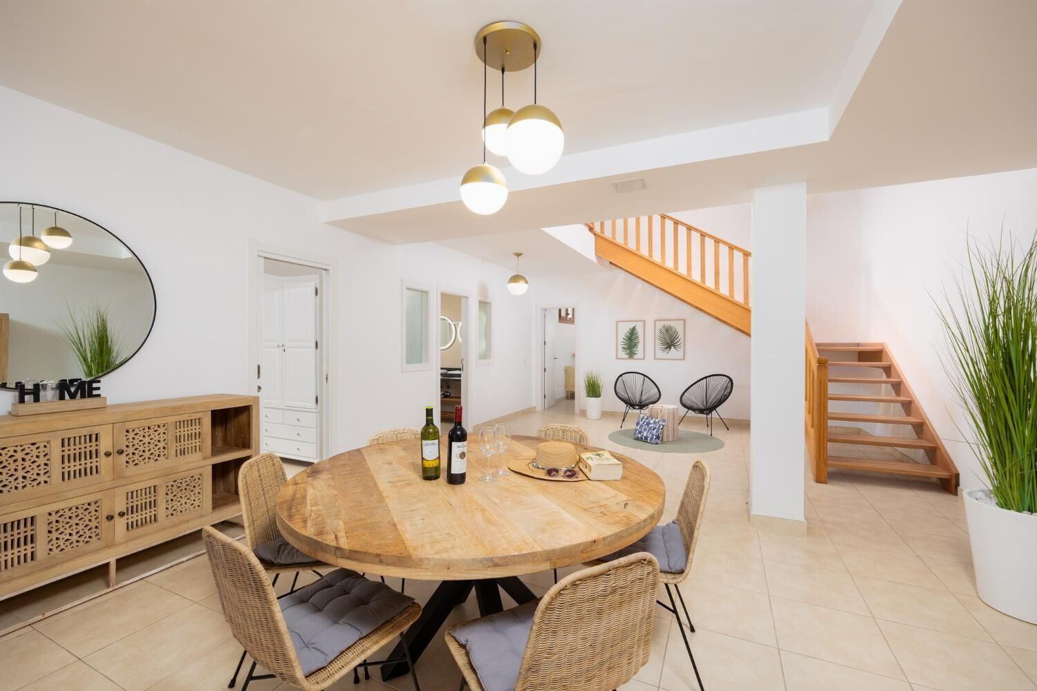Un comedor espacioso con una mesa de madera, sillas de mimbre y una escalera que lleva a un nivel superior.
