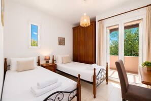 Ein Hotelzimmer mit zwei Betten, einem Holzschrank, einem kleinen Tisch mit Stuhl und einem Balkon mit Blick auf Grün.