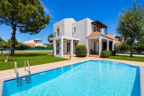 A modern house with a swimming pool, a covered outdoor area, and a well-maintained lawn.