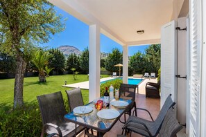 A covered patio with a table set for two, a pool, and a view of a mountain.