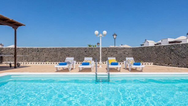En swimmingpool med solstolar och en stenmur.