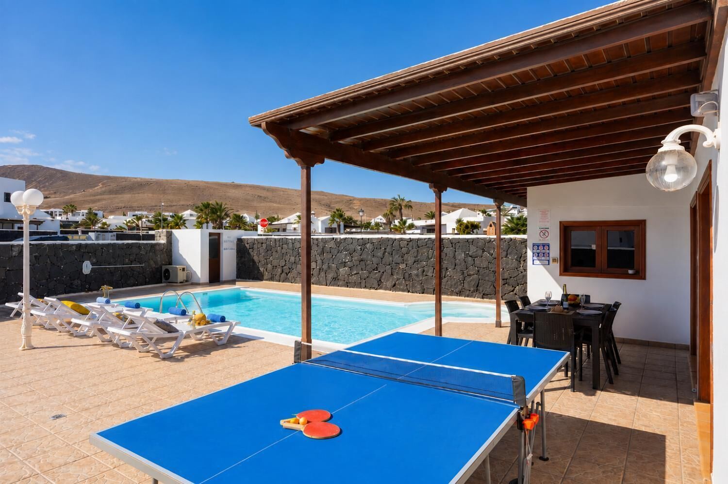 A pool area with a ping pong table, lounge chairs, and a covered seating area.