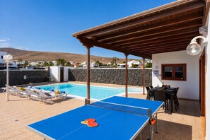 A pool area with a ping pong table, lounge chairs, and a covered seating area.